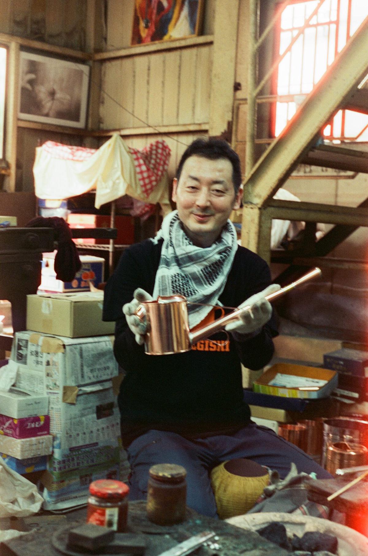 Yoichi Negishi seated in his Tokyo workshop holding a finished copper watering can