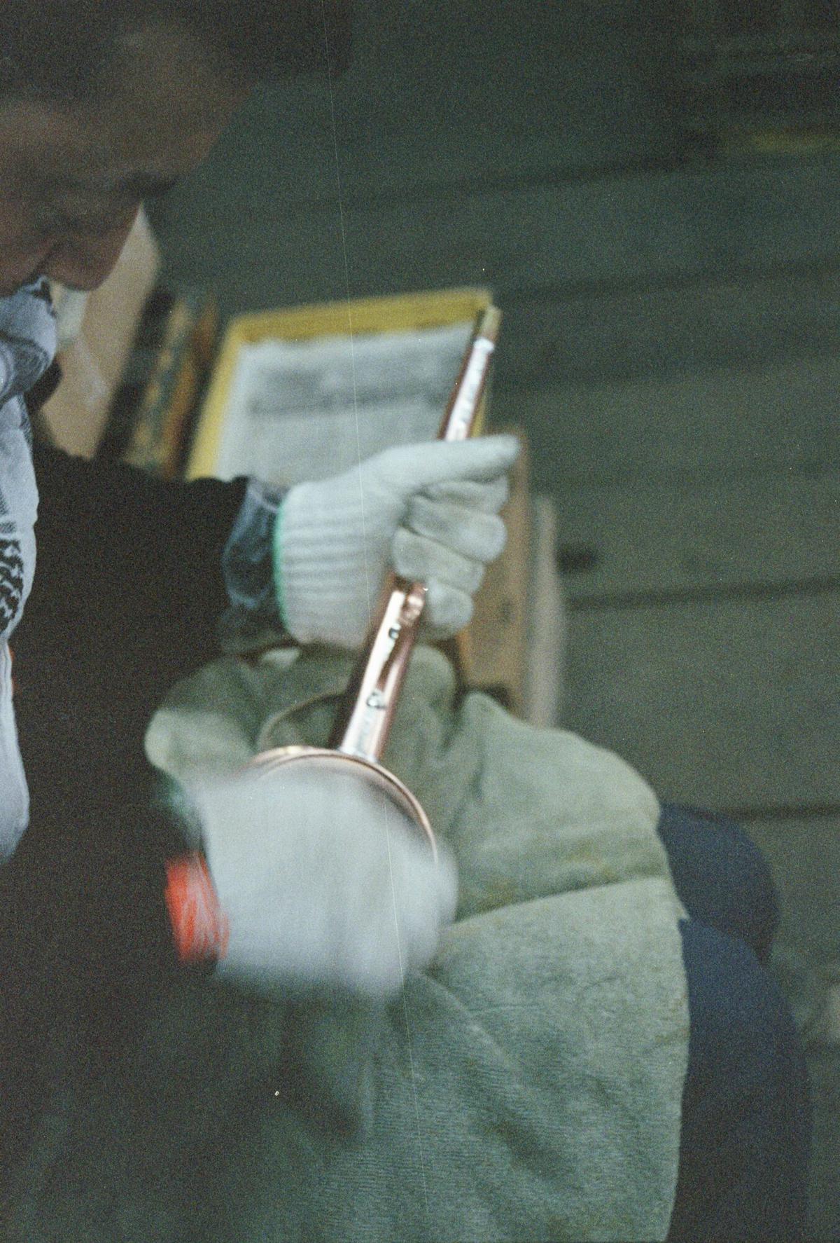 A gloved hand polishing the body of a copper watering can