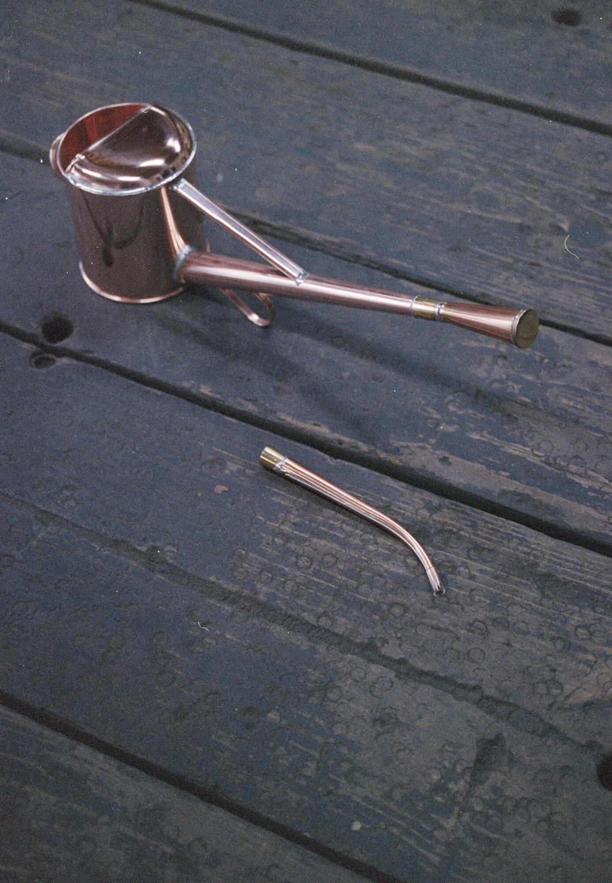 A finished copper Chooro watering can and its long spout on dark wooden boards