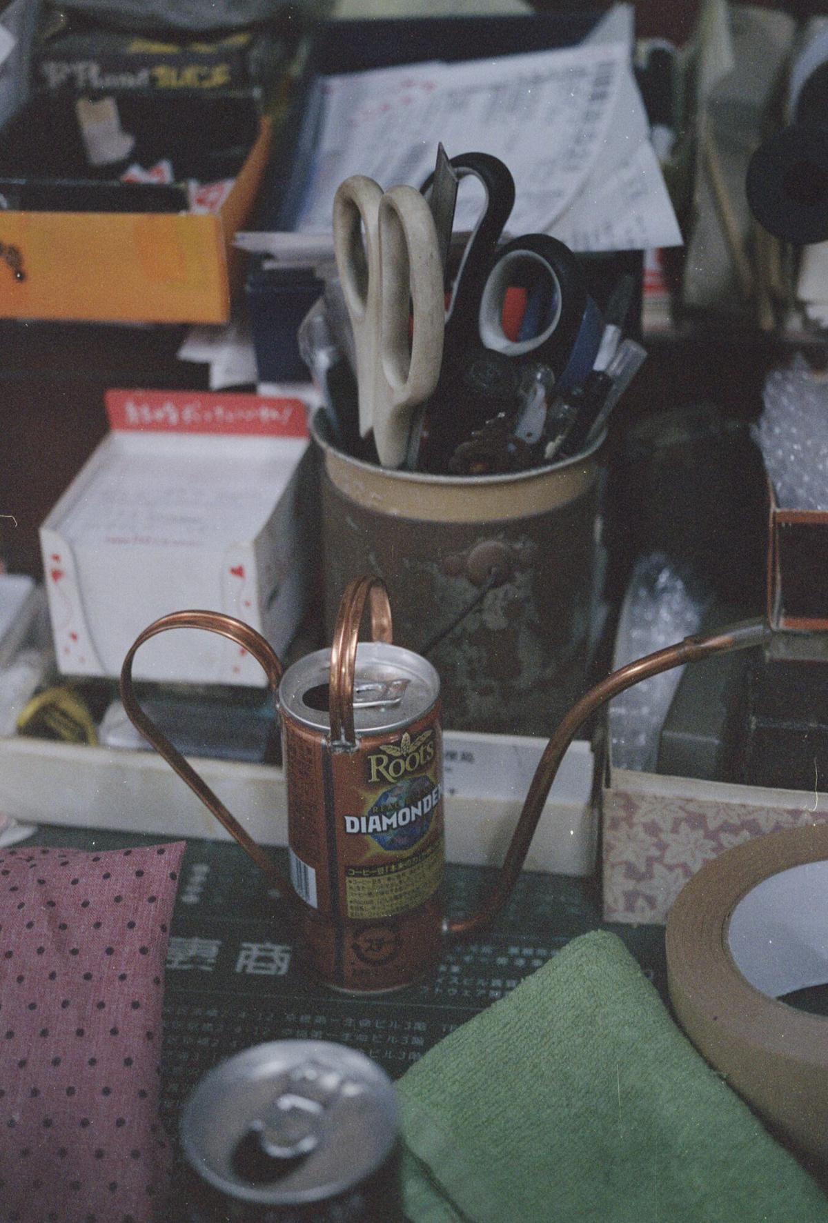 A watering can made from an empty Japanese canned coffee tin, with a copper spout and handle soldered on, standing on the workshop bench
